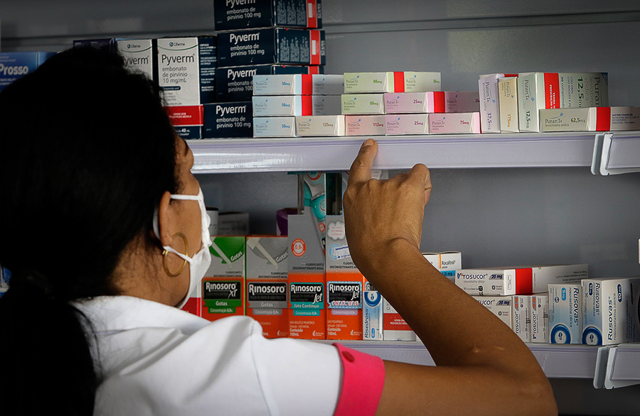 Fotografia de um farmacêutico procurando por um medicamento em uma prateleira