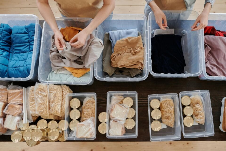 Imagem de mãos de voluntários separando doações de comida e roupas